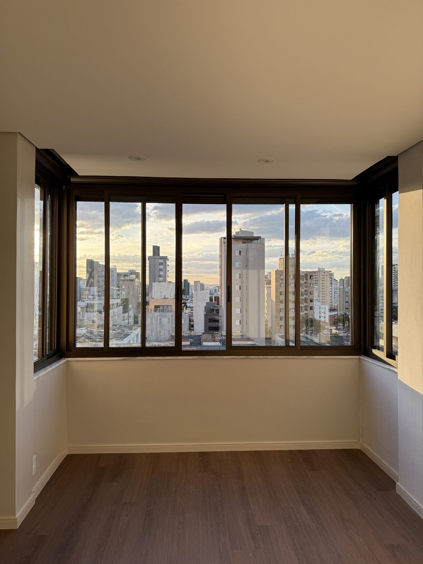 Suíte do apartamento com esquadrias panoramicas de canto, peitoril em mármore e piso em madeira