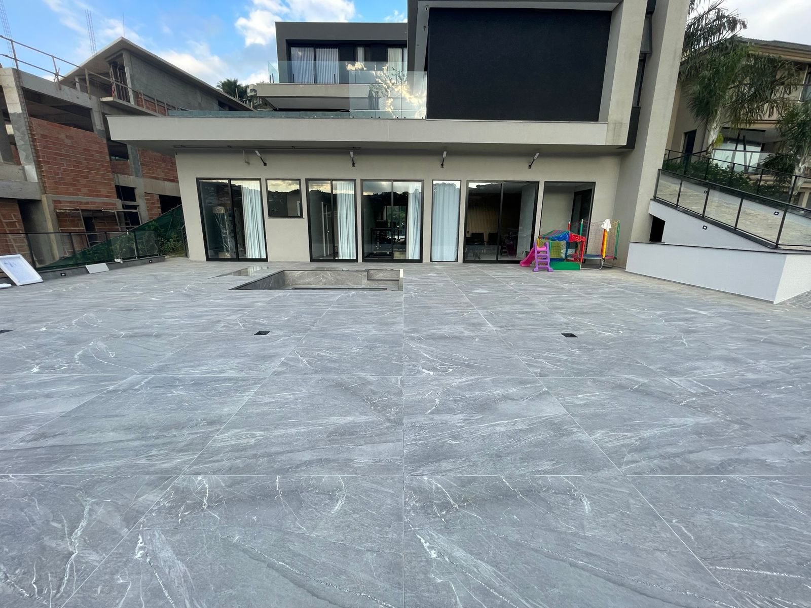 Área externa de residência de alto luxo com piso em porcelanato marmorizado de grande formato e piscina integrada ao deck, executada pela Apus Construtora