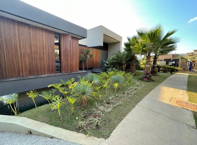 Fachada de residência de alto luxo em condomínio fechado, com brise de madeira, volumes em concreto e paisagismo, executada pela Apus Construtora